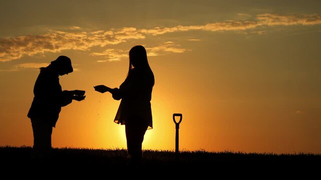 Two female farmers examining soil and discussing crop condition in agricultural field at sunset outdoors.