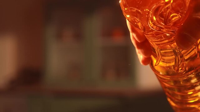 Close up of vegetable oil pouring from plastic bottle in warm kitchen light. Cooking ingredient concept with golden liquid stream, suitable for cooking at home, in a restaurant or cafe, healthy eating
