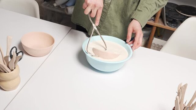 Artisan Dipping Ceramic Bowl into Glaze Basin 4K Video Slow Motion. Artisan handles an unglazed clay vessel during the manual glazing process
