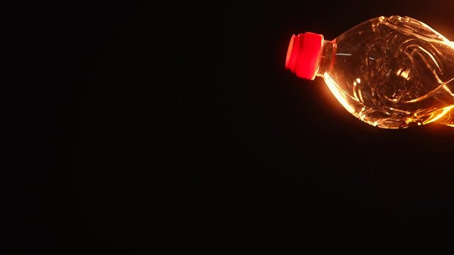 Bright golden vegetable oil pouring from plastic bottle with dramatic warm lighting on black background. Food cooking ingredient concept with copy space and glowing reflections.