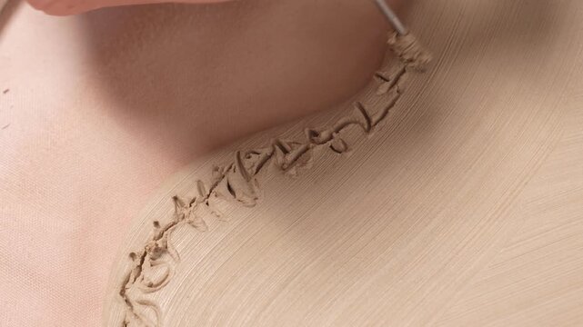 Artisan Carving Clay Texture with Tool 4K Video Slow Motion. Artist uses a sharp metal carving tool to incise a repeating decorative texture into the curved wall of a clay artwork