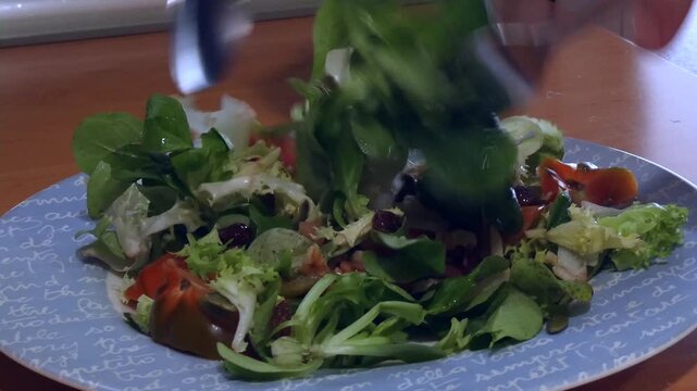 Close-up of a person tossing a healthy salad with lamb's lettuce, tomato, escarole and nuts