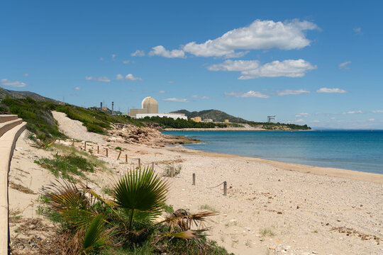 Sandy Mediterranean coastline near Tarragona with calm turquoise sea and the Vandell&ograve;s nuclear power plant visible on the horizon. Sunny coastal landscape in Catalonia, Spain with natural beach scener
