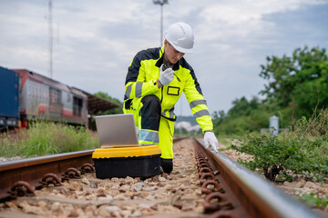 Naklejka premium Professional male industrial engineer kneeling using walkie talkie inspecting railway track with laptop on tool box for sustainable freight transport logistics and corporate supply chain business.
