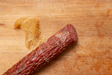 Peeling a dry pork salami on a wooden chopping board, flat lay close up © Dorin