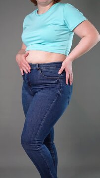 Overweight woman struggling to button too tight jeans over her belly, concept of weight gain and need for dieting