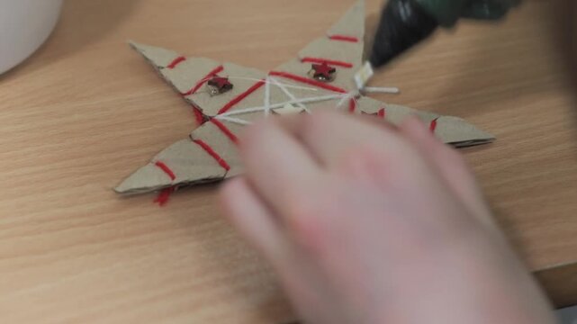 Handmade Cardboard Christmas Star Decoration with Red Thread and Wooden Beads During Holiday Crafting