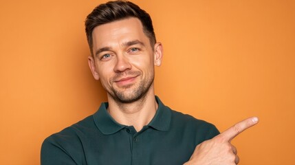 Fototapeta premium Handsome mid adult man pointing finger to side copy space looking at camera with friendly smile over orange background promotion advertisement portrait looking away single casual male guy model