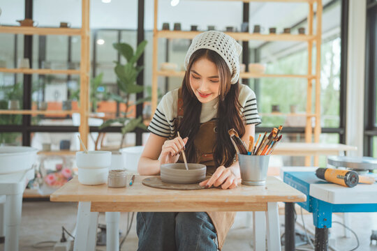 Asian woman artist painting handmade ceramic product in pottery studio &ndash; creative process of decorating sculpture with brush for small business, art workshop, and modern craft design startup