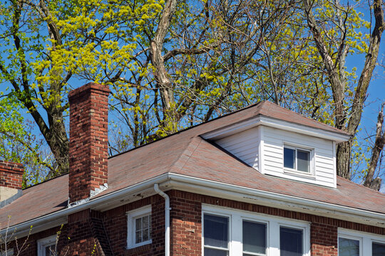 Traditional brick house roof with a prominent chimney and a white hipped dormer in Boston, Massachusetts, USA
