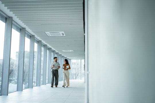 Business colleagues walking and conversing in modern office hallway