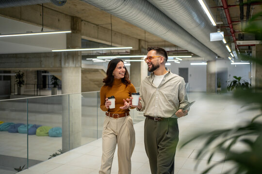 Business colleagues walking, talking, and drinking coffee in office