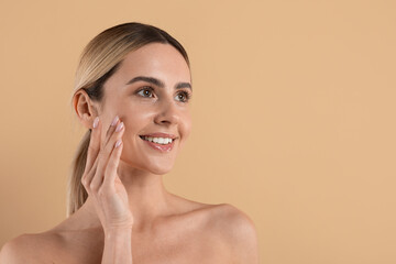 Smiling young caucasian woman with radiant healthy skin touching cheek in beauty and skincare concept isolated on clean beige studio background, copy space © Anastasiya