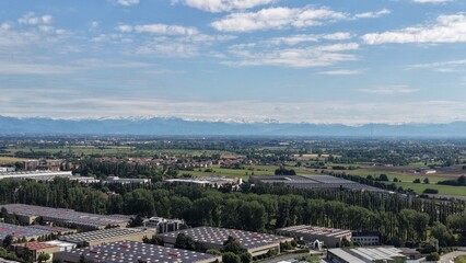 Fototapeta premium Industrial Landscape with Distant Mountains: An aerial view captures a sprawling industrial zone nestled amidst lush green trees and agricultural fields.
