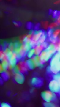 Vertical video. Shimmering flare bokeh. Spectrum glow. Colorful neon rays swirling on dark black background. Abstract rainbow purple red blur reflection.