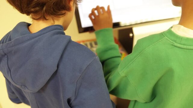 Two curious young boys engaging with an interactive touchscreen kiosk, exploring educational games and digital content in a modern library or children's museum