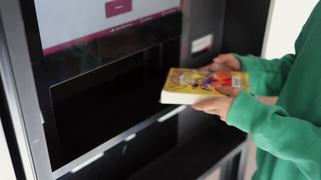 Young student using a self-service machine to return books to the public library, showcasing automated checkout system technology and modern education process concepts