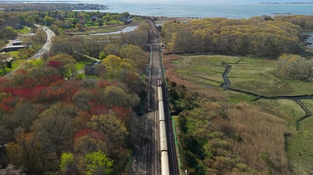 Amtrak passenger train in Mystic aerial view, a high-angle drone tracking shot following a regional train as it travels along the coastal Northeast Corridor tracks in Mystic, Connecticut.