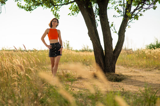 Woman in Orange Top Standing by Tree in Summer Field