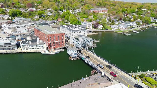 Mystic River Bascule Bridge aerial view, a high-angle drone video showing cars crossing the iconic drawbridge near downtown storefronts and the waterfront on a bright spring day in Mystic Connecticut.