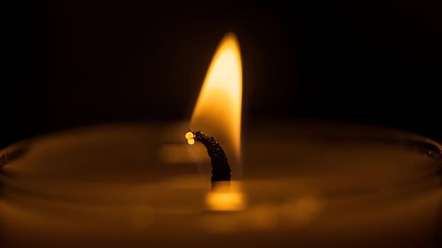 Close up of a single candle flame glowing warmly in the dark