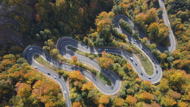 Drone perspective of serpentine roadway cutting through colorful fall forest in Maramures, Romania.