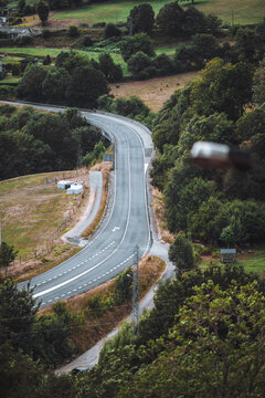 Quiet asphalt highway winding between lush rural hills, trees, fields and scattered houses, scenic countryside route for travel, road trip and landscape concepts