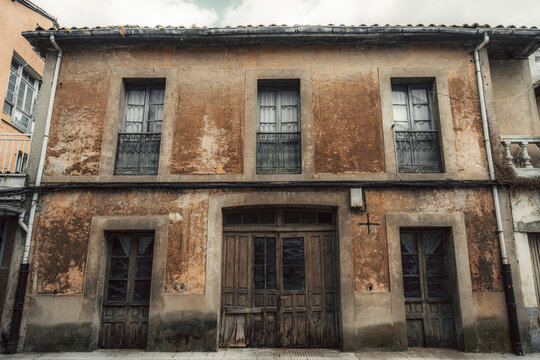 Aged plaster wall with cracked texture, worn wooden doors, curtained windows and iron balconies, rustic historic architecture detail in Asturias, Spain