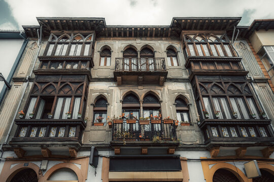 Traditional building facade with ornate dark wooden galleries, arched windows, iron railing and flower pots, historic Asturian street architecture