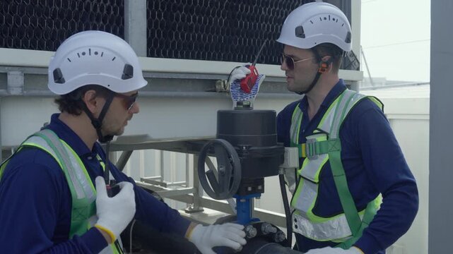 Engineer maintenance hvac cooling tower technician safety inspection and repair on rooftop plant, workers adjust valve, actuator and pipe control with radio communication, helmet, glove, earplug