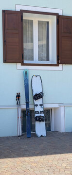 Winter sports equipment with skis and snowboard leaning against the wall of traditional alpine house with wooden shutters