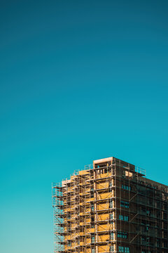 A modern urban building wrapped in scaffolding under a vibrant blue sky, conveying construction, renovation, architecture and industrial progress