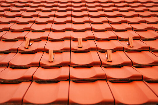 Textured terracotta roofing tiles with metallic snow guards on sloped house roof, construction detail and geometric design