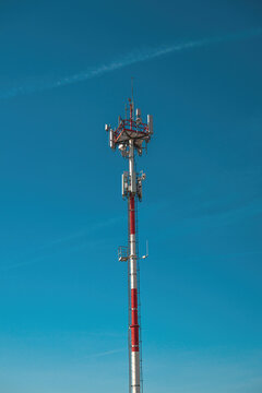 Red and white cell tower with antennas against clear blue sky for telecommunication and connectivity