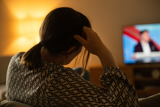 Woman sitting indoors facing TV screen in dark room, relaxation and modern media consumption concept
