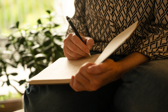 Middle-aged woman writing notes in notebook while sitting at home, reflective and productive evening scene