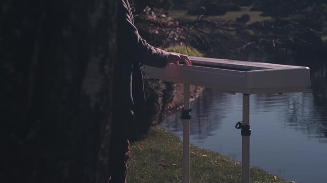Cinematic close-up of musician playing white digital piano near peaceful lake in atmospheric evening light.