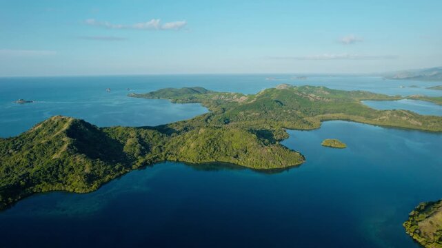 Drone shot pulling back slowly over lush green hills overlooking calm tropical bays and archipelago in Riung 17 Islands National Park, Flores.
