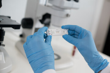 Obraz premium Horizontal view of a researcher in blue gloves holding up a rapid testing device for hantavirus inside a clean medical laboratory environment.