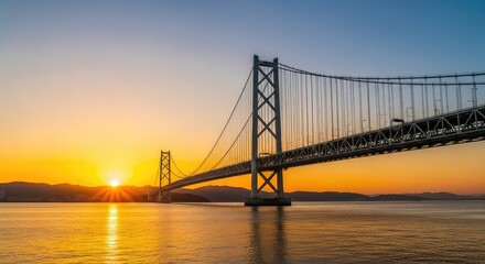 Obraz premium A majestic suspension bridge stretches across a wide river at sunset, with golden light reflecting on the calm water and clear blue sky, cables, landscape, environment