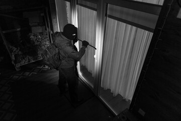 Fototapeta premium Man burglar in dark clothing trying to unlock door or window of house using crowbar