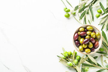 Naklejka premium Olives in wooden bowl and fresh olive tree branch at white background.