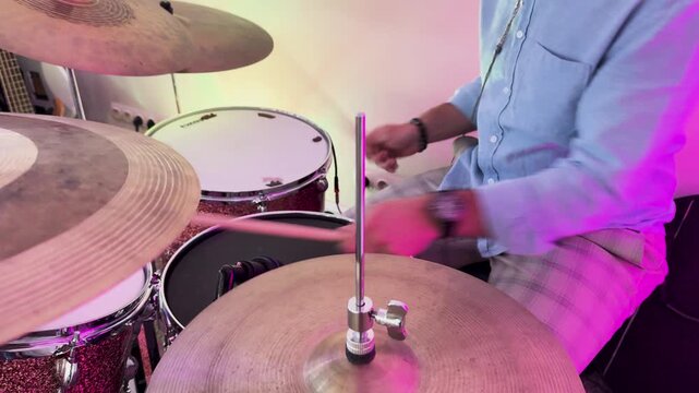 Drummer playing drum kit under pink neon stage lights