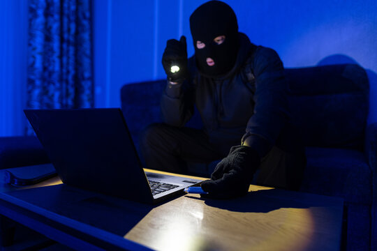 Hacker or programmer using USB flash drive for theft the information from laptop computer, sneaking into the house at night. Criminal of cyber concept