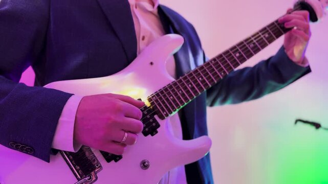 Guitarist playing white electric guitar under neon stage lights