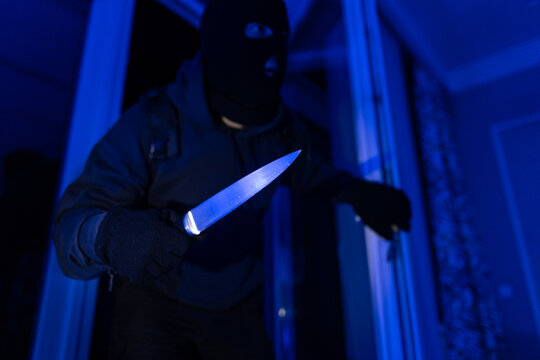 Armed burglar with knife moving carefully to private property at night, involved in covert trespassing and possible violent crime