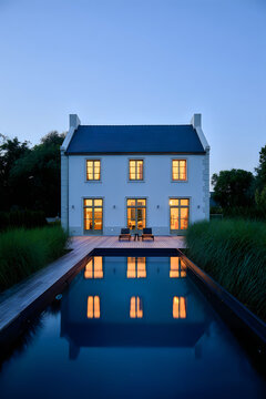 Modern house with illuminated reflecting in a dark swimming pool at dusk