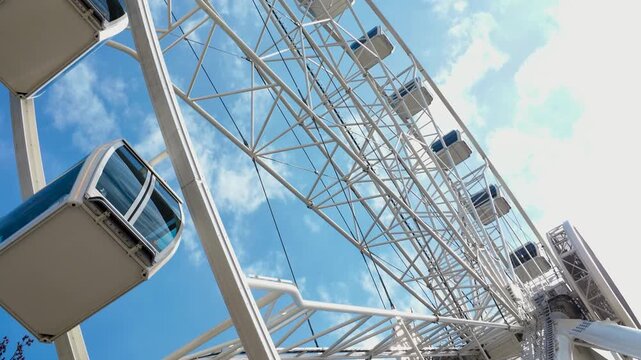 Modern Ferris Wheel Cabins: Low Angle View of Observation Wheel with White Steel Structure and Blue Sky Background