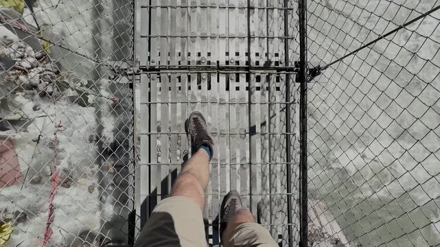 POV shot of hiker crossing suspension bridge over Himalayan river in Nepal