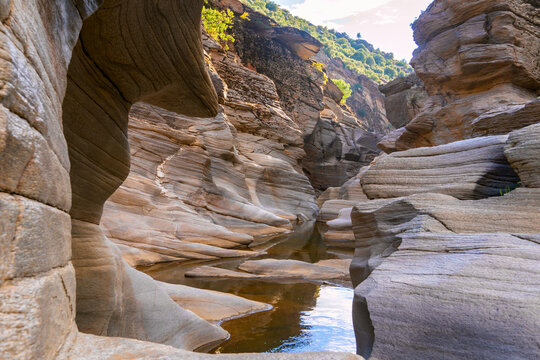 Narrow canyon with layered rock formations and small stream flowing through eroded stone landscape. Natural geological scenery shaped by water erosion in remote wilderness area